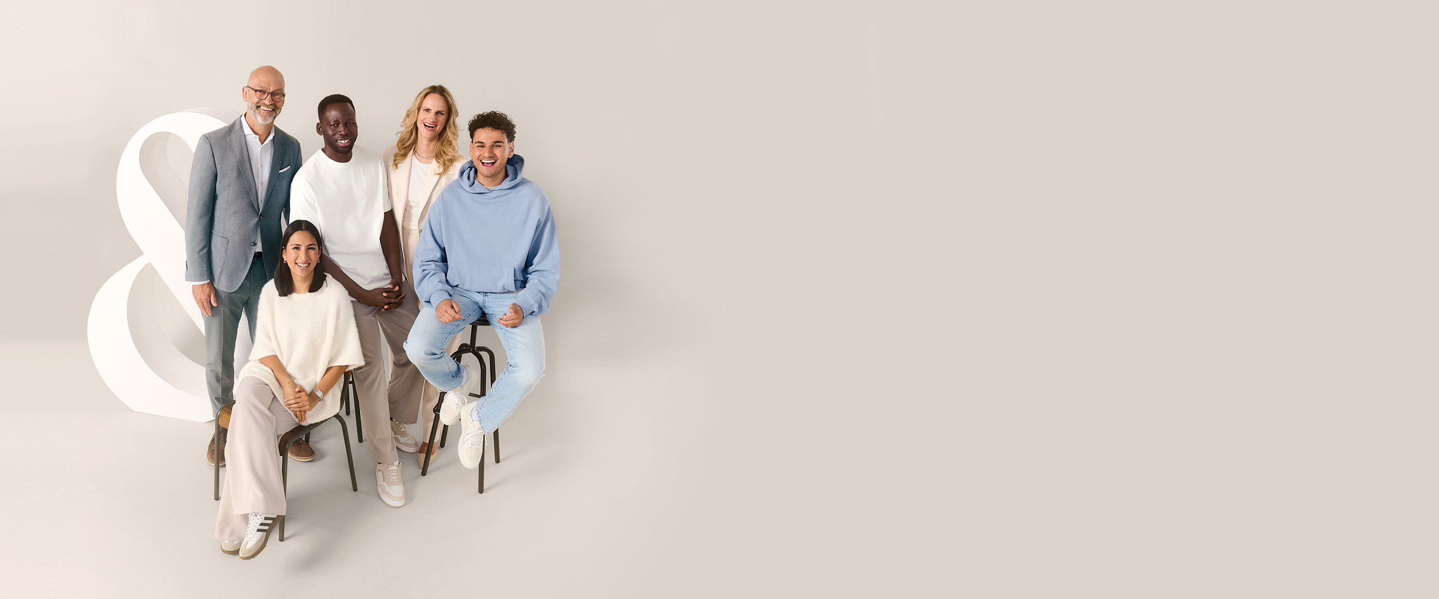 Eine Gruppe Menschen verschiedenen Alters und Geschlechts stehen vor einem beigen Hintergrund neben einem "Et-Zeichen".